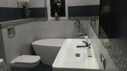 Nowoczesna łazienka z wolnostojącą wanną, białą umywalką i mozaiką. Minimalistyczny design z akcentami czerni i kwiatami w wazonie.