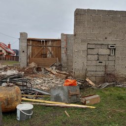 MARCIN MICAŁ - Po rozbiórce: fragment muru z pustaków, drewniana brama i gruzowisko na trawie. W tle dom z czerwoną dachówką pod pochmurnym niebem.