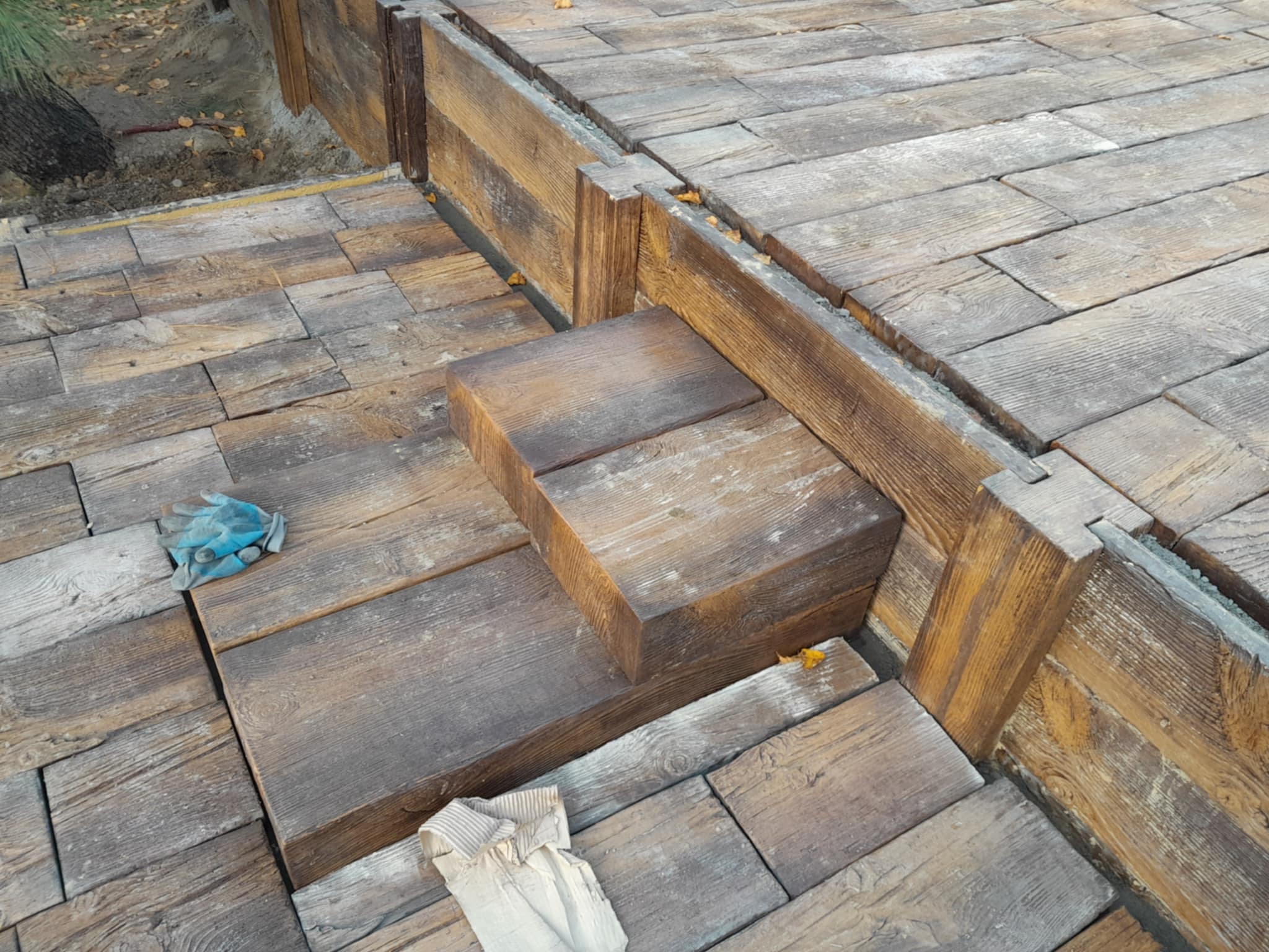 Ułożona kostka brukowa imitująca drewno, tworząca schody i podest w Rzeszowie. Widoczne rękawice robocze i elementy wykończeniowe.