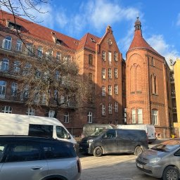 SegmentPRO - Dom Prowincjalny Zgromadzenia Sióstr św. Elżbiety w Poznaniu. Czerwona cegła, wieżyczka z krzyżem, okna z białymi ramami. Widok z ulicy, zaparkowane samochody.