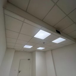 SegmentPRO - Białe, kasetonowe wykończenie sufitu z wbudowanym oświetleniem w jasnym pomieszczeniu biurowym. Widoczna biała ściana i drzwi.