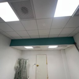 SegmentPRO - Wnętrze biura w trakcie wykańczania: podwieszany sufit z oświetleniem, pomalowana na turkusowo ściana, zabezpieczone drzwi i sprzęt budowlany.