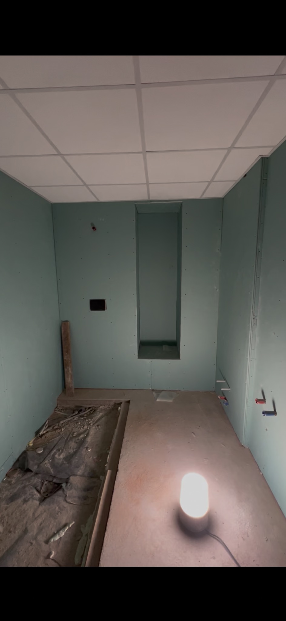 Łazienka w trakcie remontu: ściany obłożone płytami gipsowo-kartonowymi, widoczna wnęka w ścianie, sufit podwieszany. Na podłodze resztki materiałów budowlanych.