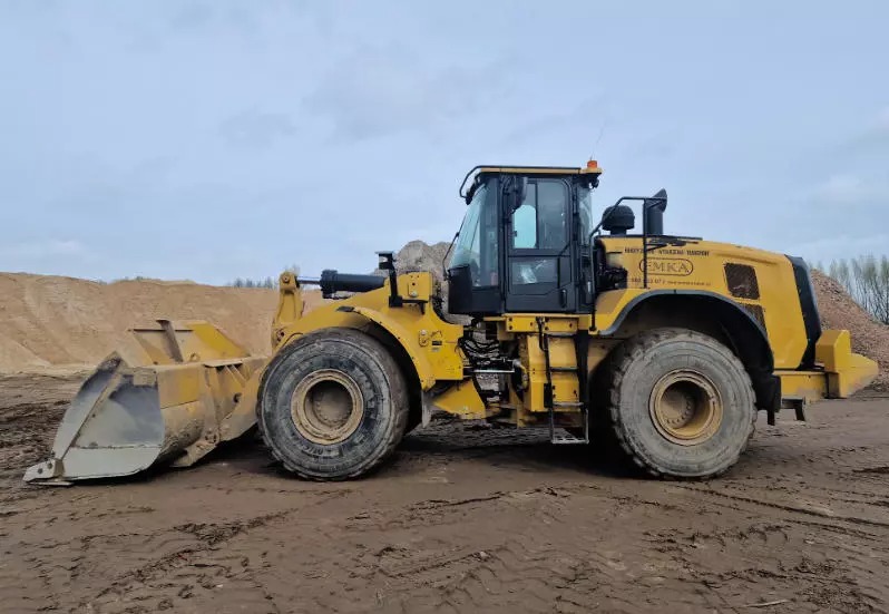 Żółta ładowarka kołowa na placu budowy, z widoczną stertą piasku w tle. Maszyna z logo firmy EMKA, gotowa do pracy przy robotach ziemnych.