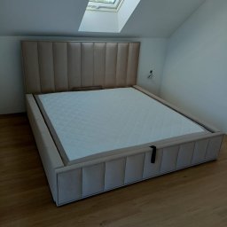 Sprzedaż Mebli Konrad Wójcik - Beżowe, tapicerowane łóżko z pikowanym zagłówkiem w nowoczesnej sypialni z oknem dachowym. Widoczny fragment podłogi z paneli.