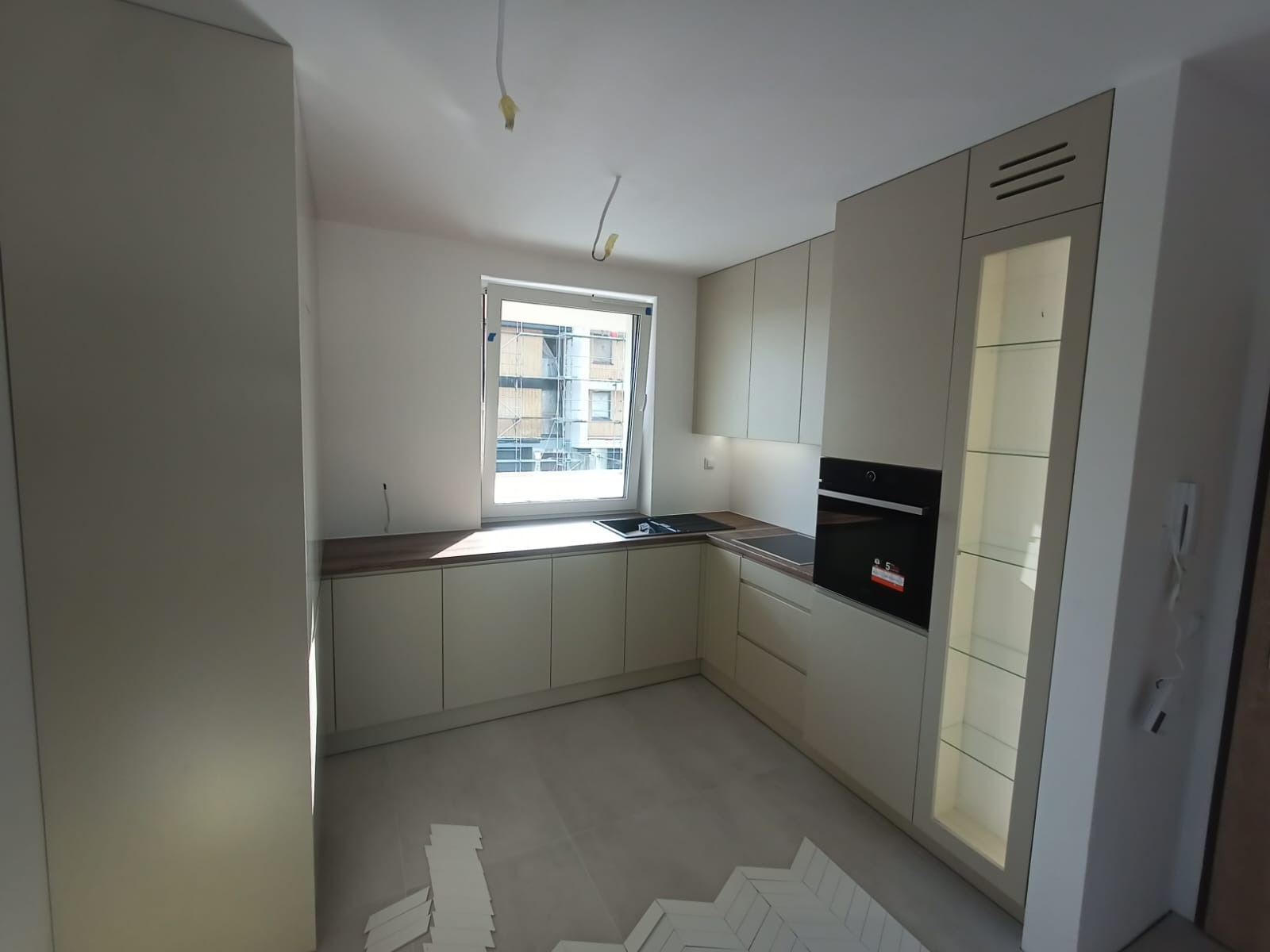 Jasna kuchnia z drewnianym blatem, jeszcze w trakcie wykańczania, z widocznymi płytkami na podłodze i wystającymi kablami, w nowoczesnym stylu.