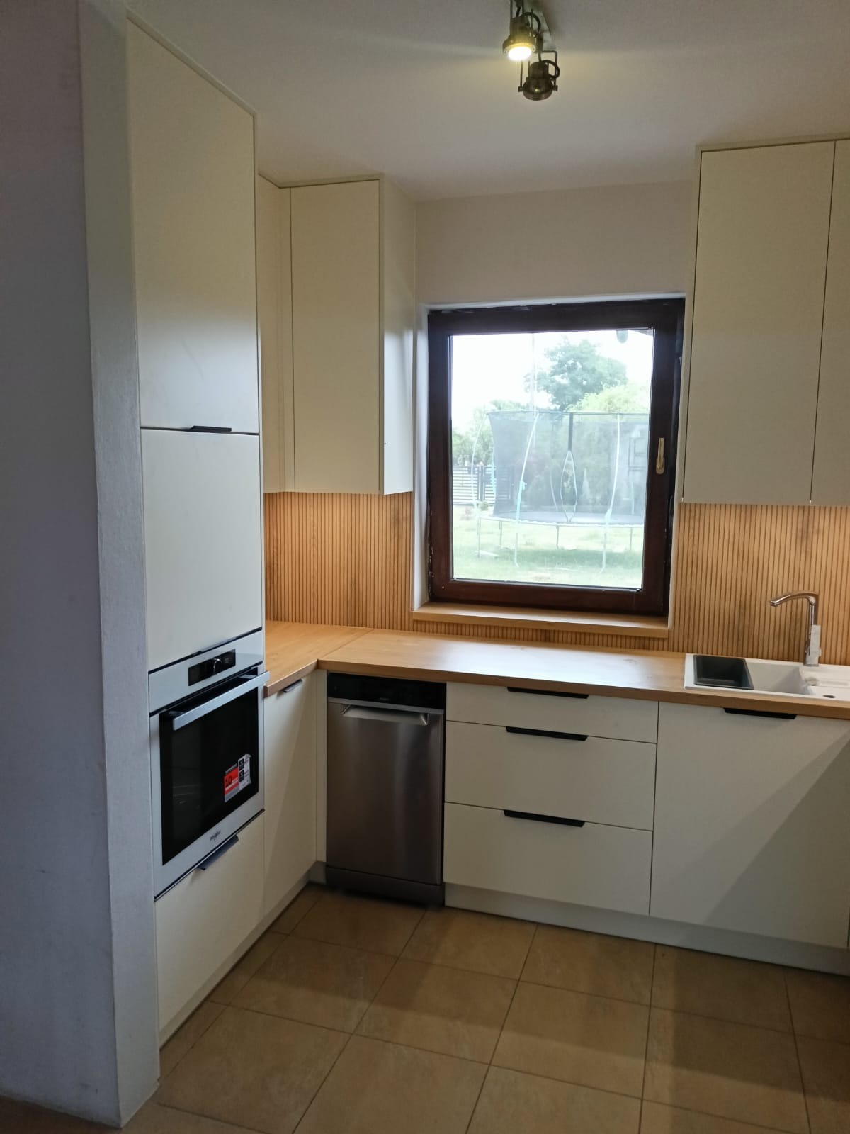 Jasna kuchnia z drewnianym blatem i panelem ściennym w Miętnem. Zabudowa kuchenna z piekarnikiem, zlewem i oknem z widokiem na ogród. Minimalistyczny design.