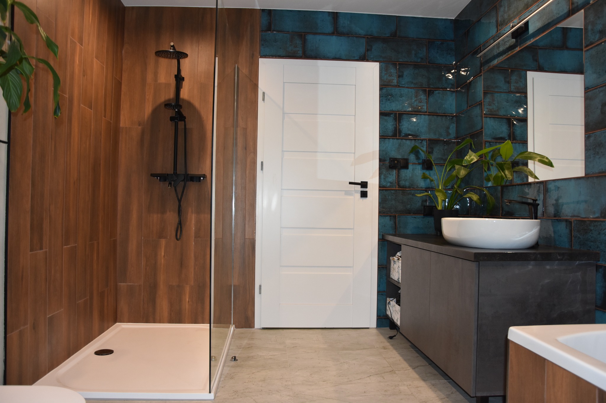 Nowoczesna łazienka z kabiną prysznicową typu walk-in, drewnopodobnymi i turkusowymi płytkami, białą umywalką nablatową i drzwiami z czarnymi akcentami.