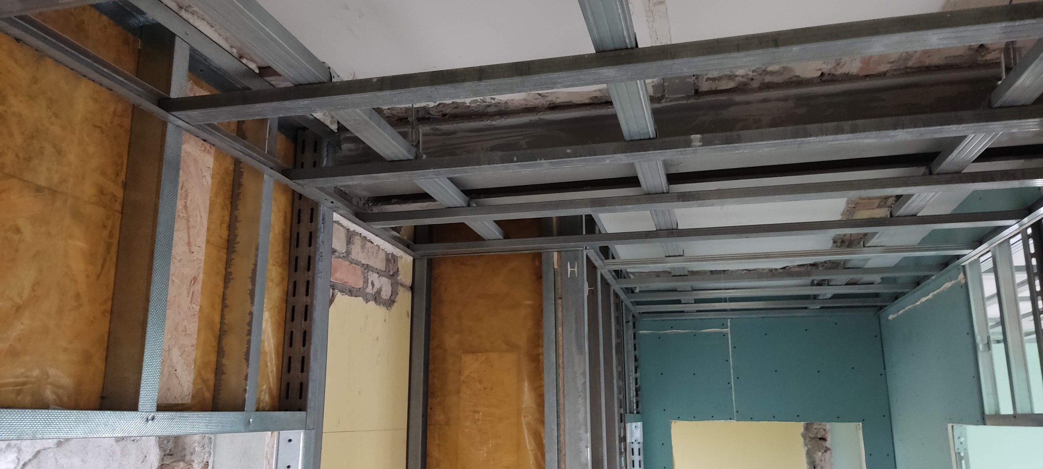 Montaż sufitu podwieszanego i ścian działowych z płyt gipsowo-kartonowych na metalowej konstrukcji. Widoczna izolacja termiczna ścian. Etap prac wykończeniowych.