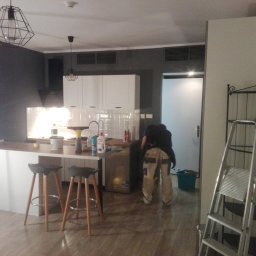 SUNSHINE SPÓŁKA Z OGRANICZONĄ ODPOWIEDZIALNOŚCIĄ - Wnętrze kuchni w trakcie prac wykończeniowych. Widoczny pracownik w trakcie pracy, drabina, farby i akcesoria malarskie. Nowoczesne oświetlenie i wykończenie.