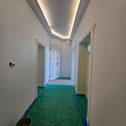 SUNSHINE SPÓŁKA Z OGRANICZONĄ ODPOWIEDZIALNOŚCIĄ - Białe, odświeżone wnętrze korytarza z trzema parami drzwi, zabezpieczone folią malarską. Sufit z podświetleniem LED. Gładkie ściany po malowaniu.