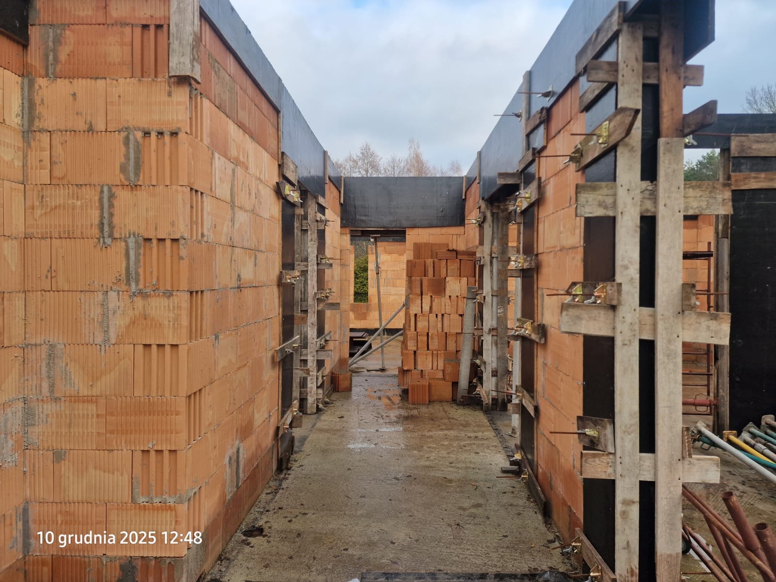 Wnętrze budowy domu z pustaków ceramicznych, widoczne szalunki i podpora. Surowy stan, przygotowanie do dalszych prac budowlanych.