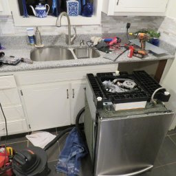 GTX SERVICE SP. Z O.O. SPÓŁKA KOMANDYTOWA - Rozłożona zmywarka z widocznymi elementami wewnętrznymi, narzędzia i akcesoria na blacie kuchennym. Widoczny etap naprawy urządzenia.