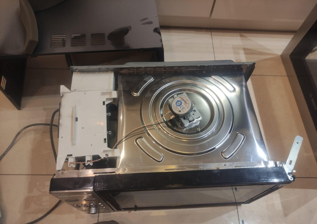 Wnętrze piekarnika Bosch z widocznym elementem grzejnym i modułem sterującym, ukazujące etap naprawy lub konserwacji. Widoczne przewody i elementy mocujące.