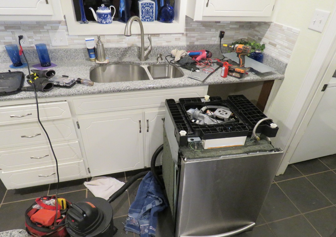 Rozłożona zmywarka z widocznymi elementami wewnętrznymi, narzędzia i akcesoria na blacie kuchennym. Widoczny etap naprawy urządzenia.