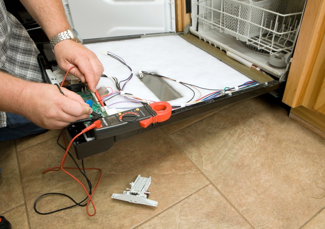 Serwisant w Warszawie diagnozuje usterkę zmywarki za pomocą multimetru. Otwarta obudowa, widoczne przewody i elementy elektroniczne.