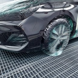 ZAKŁAD USŁUGOWO-HANDLOWO-PRODUKCYJNY Henryk Kasprzak AUTO SERVICE - Częściowo zakryty folią, czarny samochód w kabinie lakierniczej, przygotowany do malowania. Widoczna kratka podłogowa.