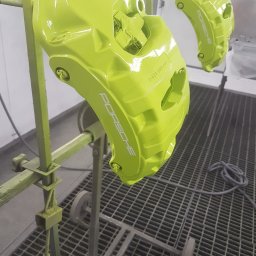 ZAKŁAD USŁUGOWO-HANDLOWO-PRODUKCYJNY Henryk Kasprzak AUTO SERVICE - Pomalowane na jaskrawozielono zaciski hamulcowe Porsche, zawieszone na stojaku w lakierni. Widoczny napis Porsche na zacisku.