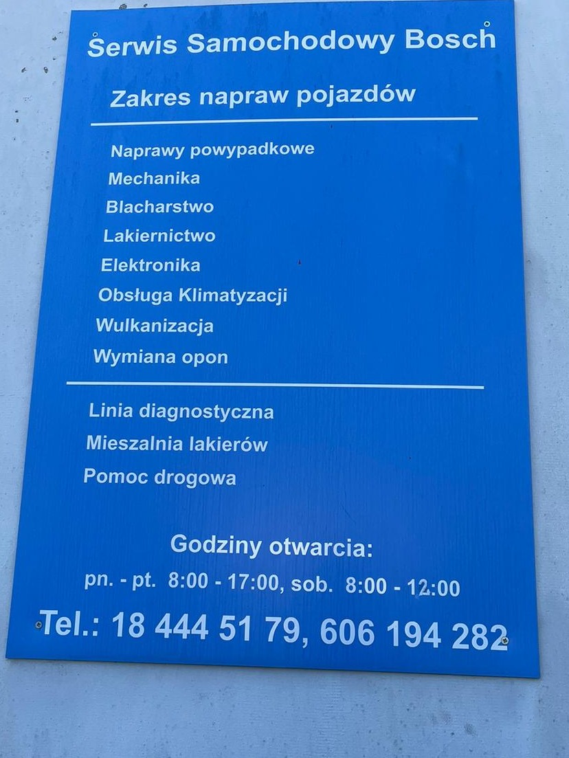 Niebieska tablica informacyjna serwisu samochodowego Bosch z zakresem usług: mechanika, blacharstwo, lakiernictwo, klimatyzacja, wulkanizacja i godziny otwarcia.
