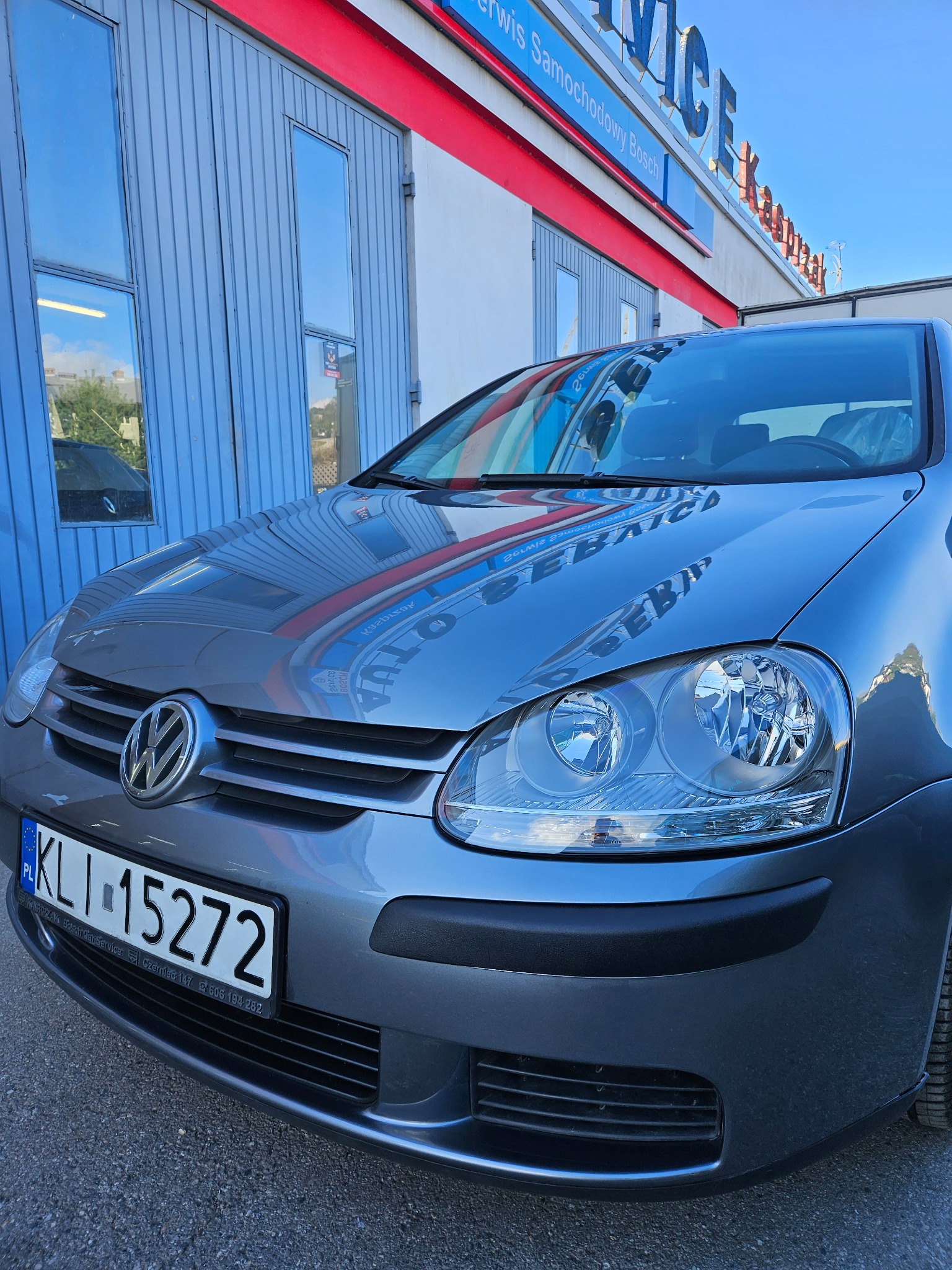 Szary Volkswagen Golf V przed warsztatem Bosch Service z widocznym numerem rejestracyjnym KLI 15272 i odbiciem szyldu w karoserii.
