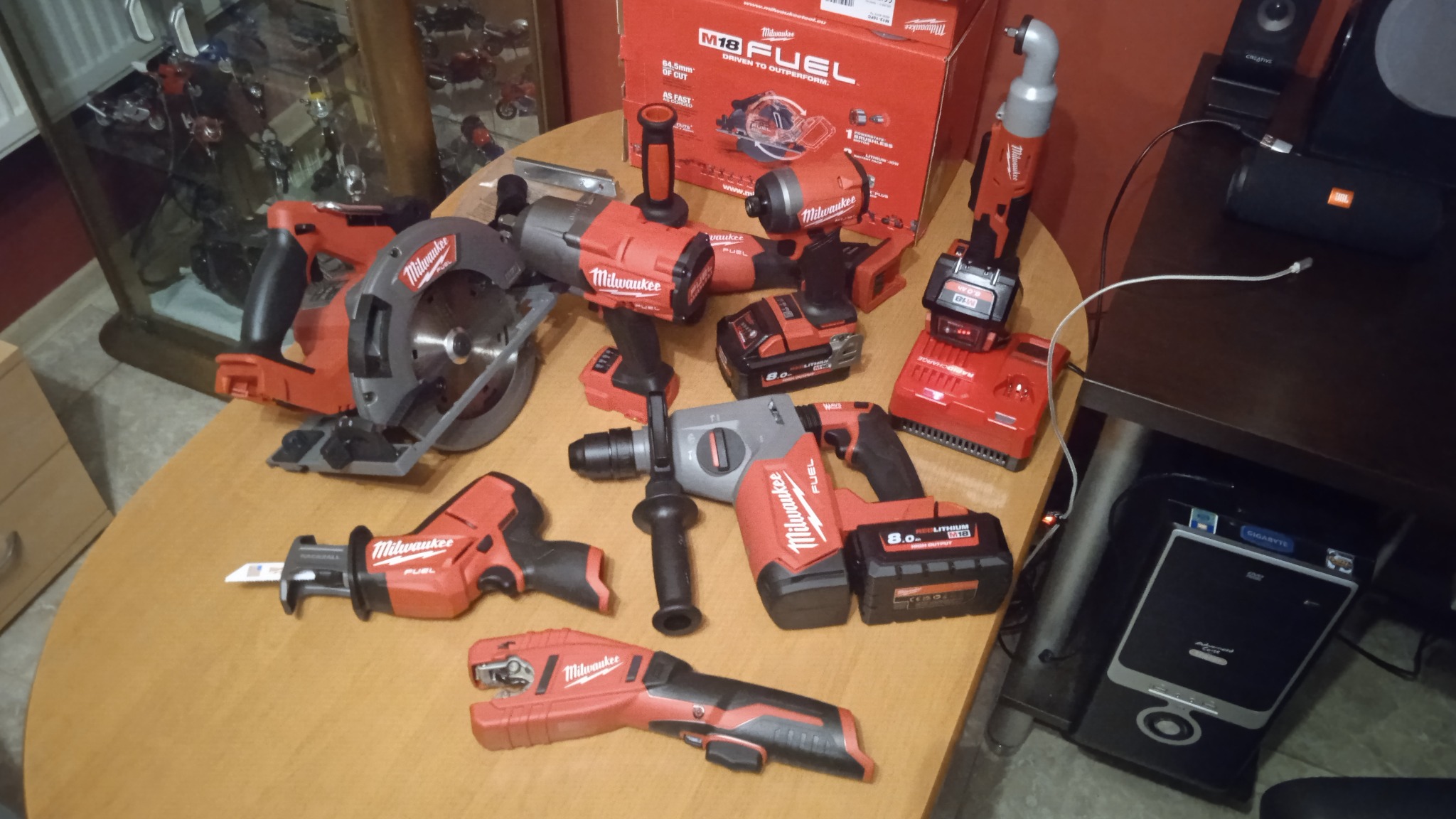 Zestaw narzędzi akumulatorowych Milwaukee M18 Fuel: piła tarczowa, młotowiertarka, piła szablasta, klucz udarowy, obcinak do rur i ładowarka. Czerwono-szara kolorystyka.