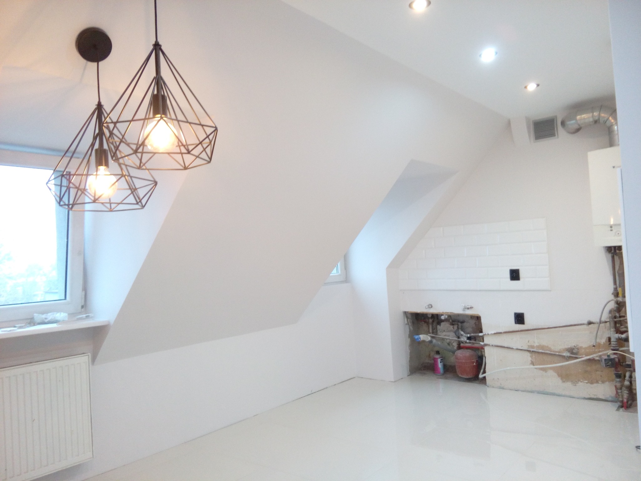 Poddasze po remoncie z białymi ścianami, nową instalacją grzewczą i designerskimi lampami wiszącymi. Widoczne elementy instalacji przed zabudową.