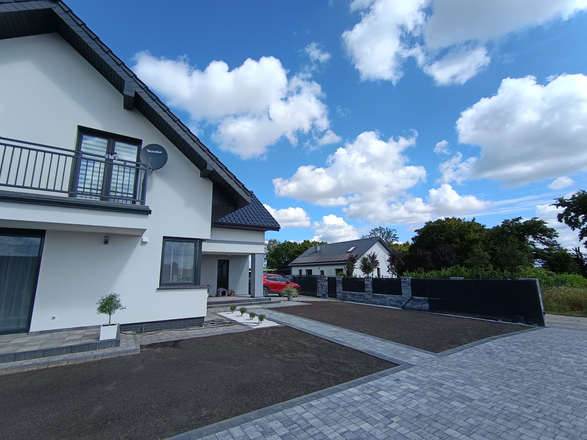 Nowoczesny dom jednorodzinny z szarą kostką brukową na podjeździe i świeżo przygotowanym trawnikiem, błękitne niebo z chmurami w tle.