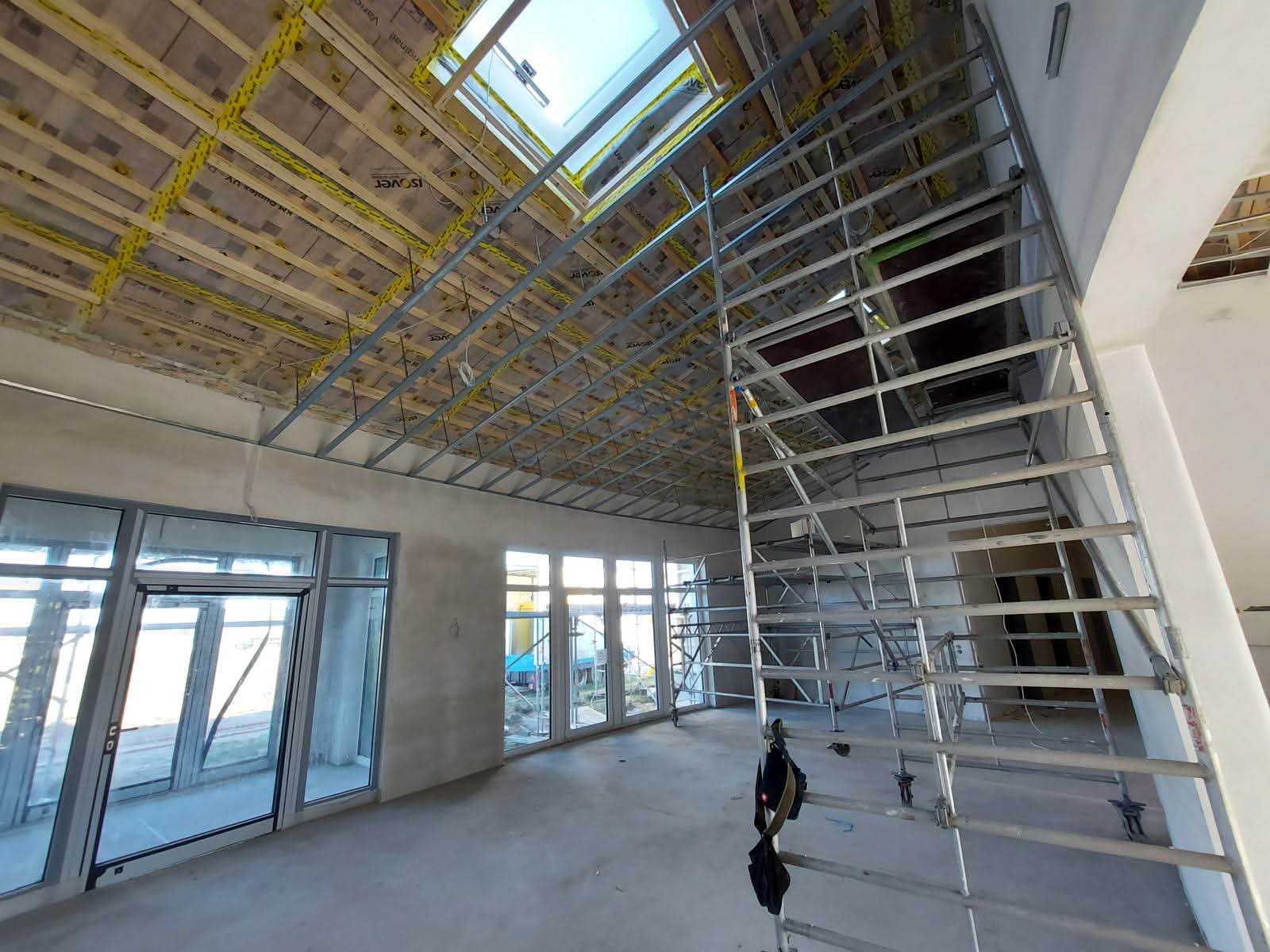 Montaż sufitu podwieszanego z płyt karton-gips w Gierałtowicach. Widoczne rusztowanie, okno dachowe i izolacja. Prace wykończeniowe w nowym budynku.