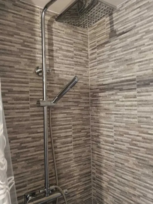 Nowoczesny prysznic z deszczownicą i szarą, poziomą mozaiką na ścianach. Chromowana armatura, minimalistyczny design. Widok na kabinę prysznicową.