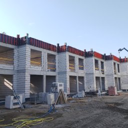 REA CAPITAL GROUP SPÓŁKA Z OGRANICZONĄ ODPOWIEDZIALNOŚCIĄ - Budowa bliźniaka z szarej cegły silikatowej, widoczne szalunki stropowe w kolorze czerwonym, na placu budowy stoi żuraw.