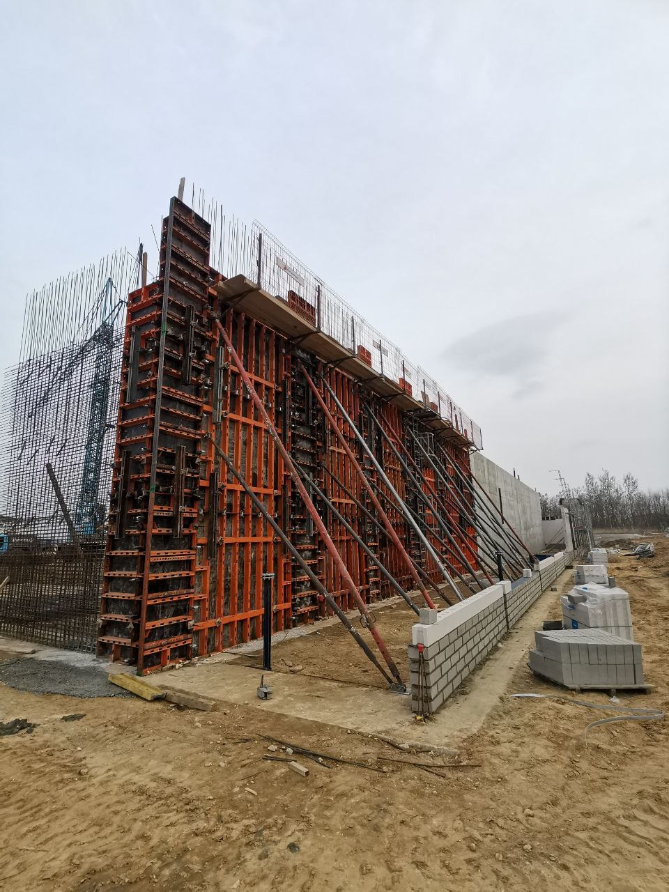 Szalunek zbrojeniowy z widoczną siatką zbrojeniową i podporami, przygotowany do zalania betonem. W tle widoczny teren budowy i pochmurne niebo.