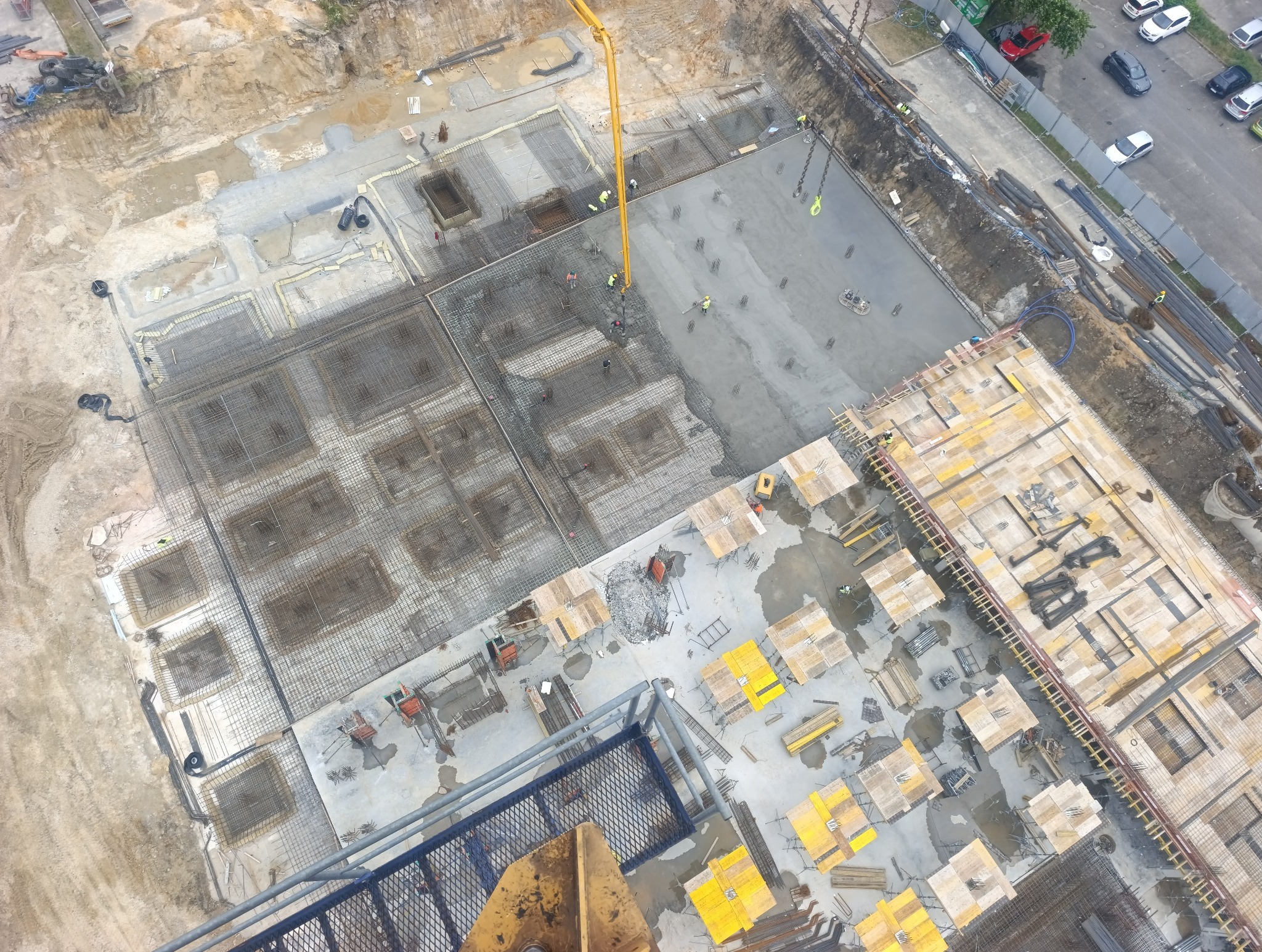 Zalewanie betonem fundamentów zbrojonych na budowie z użyciem pompy do betonu, widok z góry. Część fundamentów już zalana, część w trakcie przygotowania.