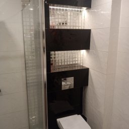 MARIUSZ WÓJCIK Remonty - Nowoczesna łazienka z kabiną prysznicową, czarno-białymi płytkami i podświetlanymi wnękami. Uwagę przykuwa geometryczny wzór płytek na ścianie i minimalistyczna toaleta.