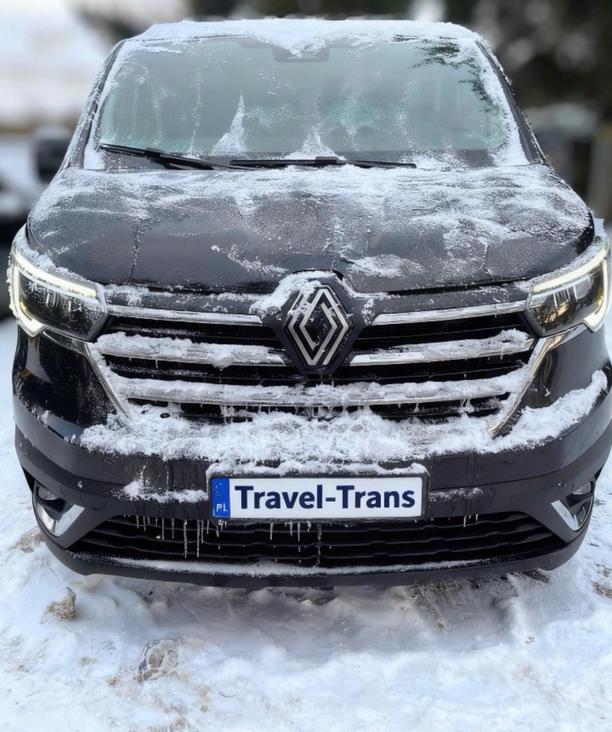 Czarny bus Renault z tablicą 'Travel-Trans' pokryty śniegiem i lodem, widok z przodu, oświetlenie LED, zimowa sceneria.