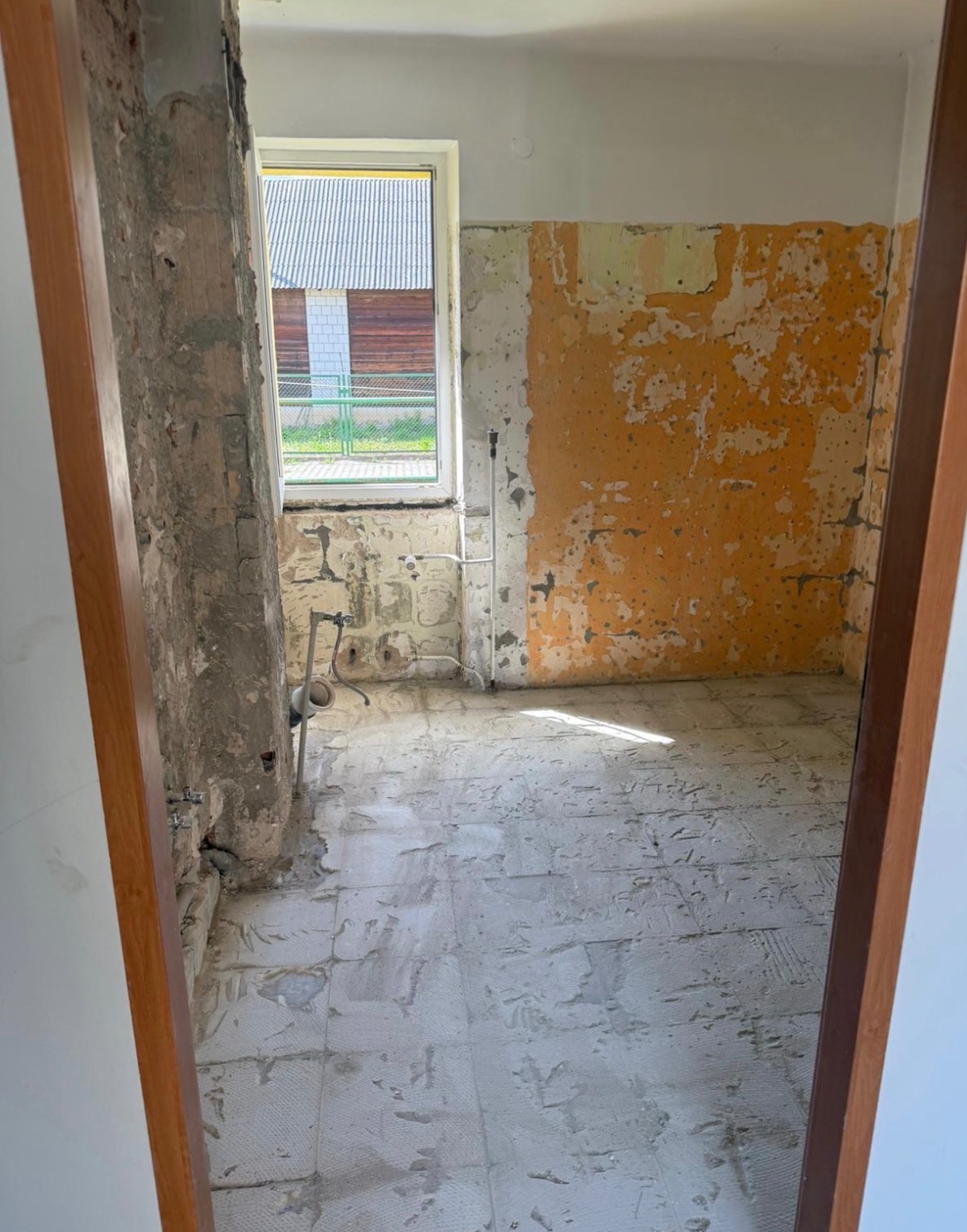 Wnętrze po częściowej rozbiórce: odsłonięta cegła, fragmenty starej farby na ścianach, zdemontowane płytki podłogowe, widok na budynek przez okno. Prace wyburzeniowe w toku.