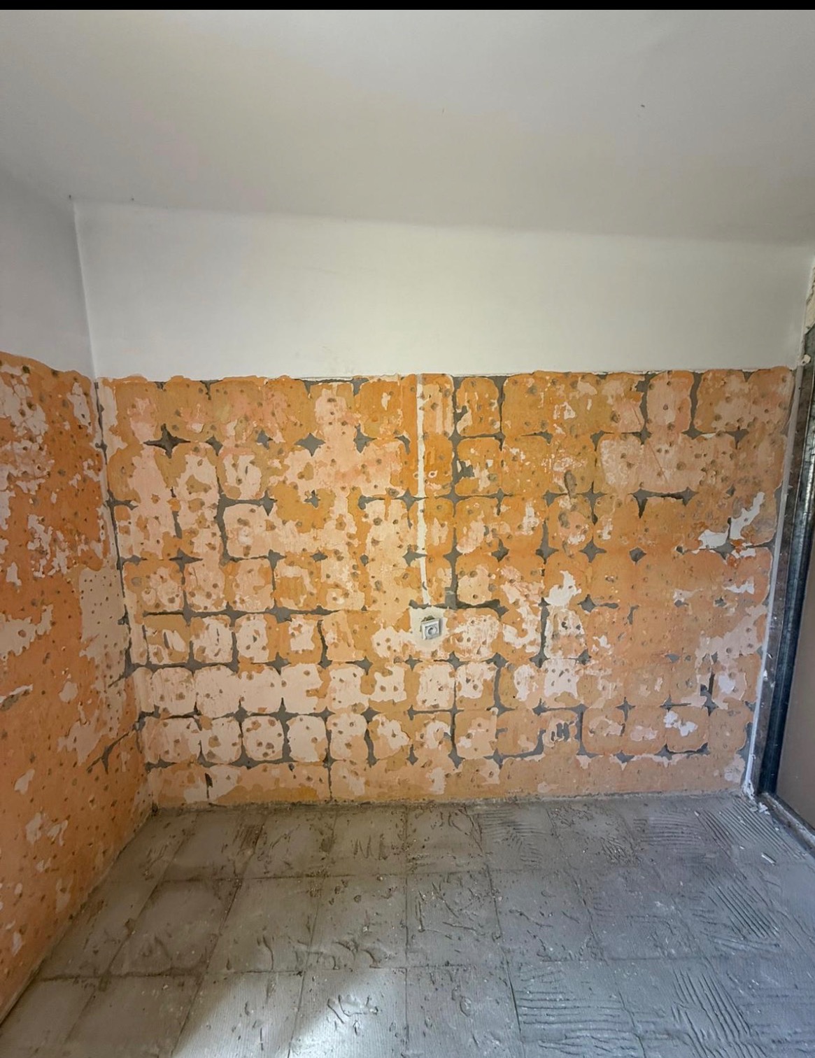 Odsłonięta ściana z resztkami płytek w pomieszczeniu po skuciu, widoczne ślady kleju i instalacji elektrycznej. Prace w toku w Wierzbicy.