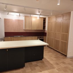 BOGUSŁAW KROPACZ - Jasna kuchnia z drewnianymi szafkami, różową mozaiką nad blatem i czarną wyspą na parkiecie w kwadraty. Oświetlenie szynowe z reflektorami.