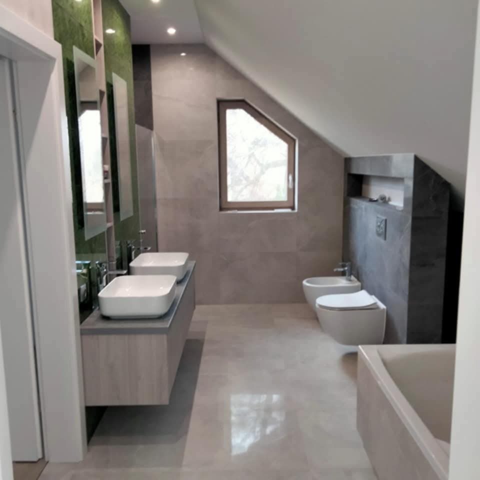 Nowoczesna łazienka na poddaszu z dwoma umywalkami, bidetem i oknem w skosie. Szare płytki imitujące marmur, minimalistyczny design, oświetlenie punktowe.