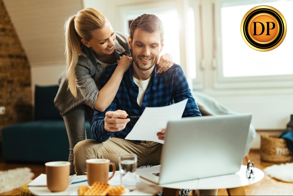 Uśmiechnięta para analizuje dokumenty przy laptopie w jasnym wnętrzu. Kobieta obejmuje mężczyznę, na stole kawa i przekąski. Logo firmy w prawym górnym rogu.