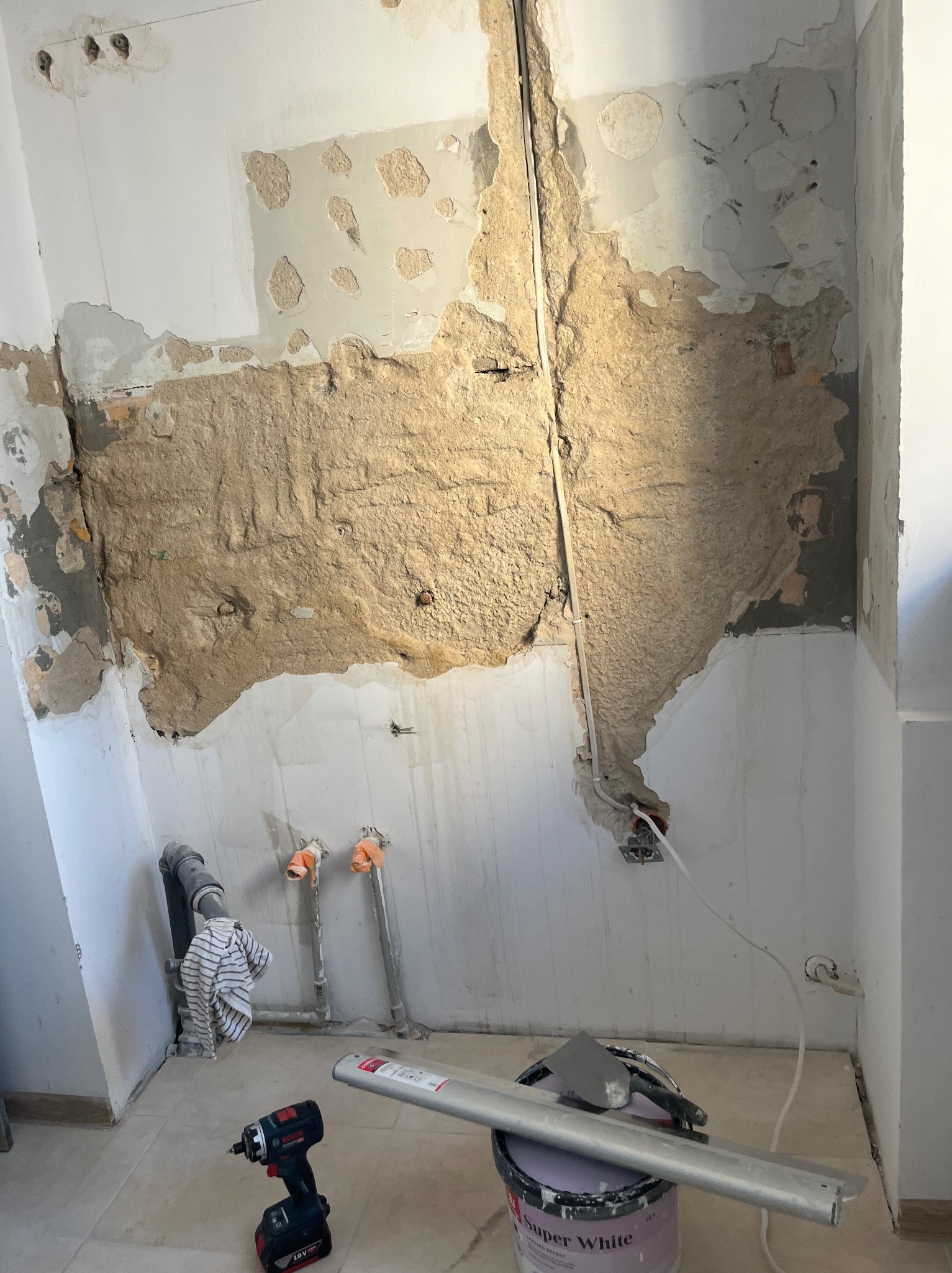 Ściana w trakcie remontu w Kazimierzu Biskupim: usunięte stare warstwy, widoczne instalacje, przygotowanie do dalszych prac wykończeniowych. Wiadro z farbą i narzędzia.