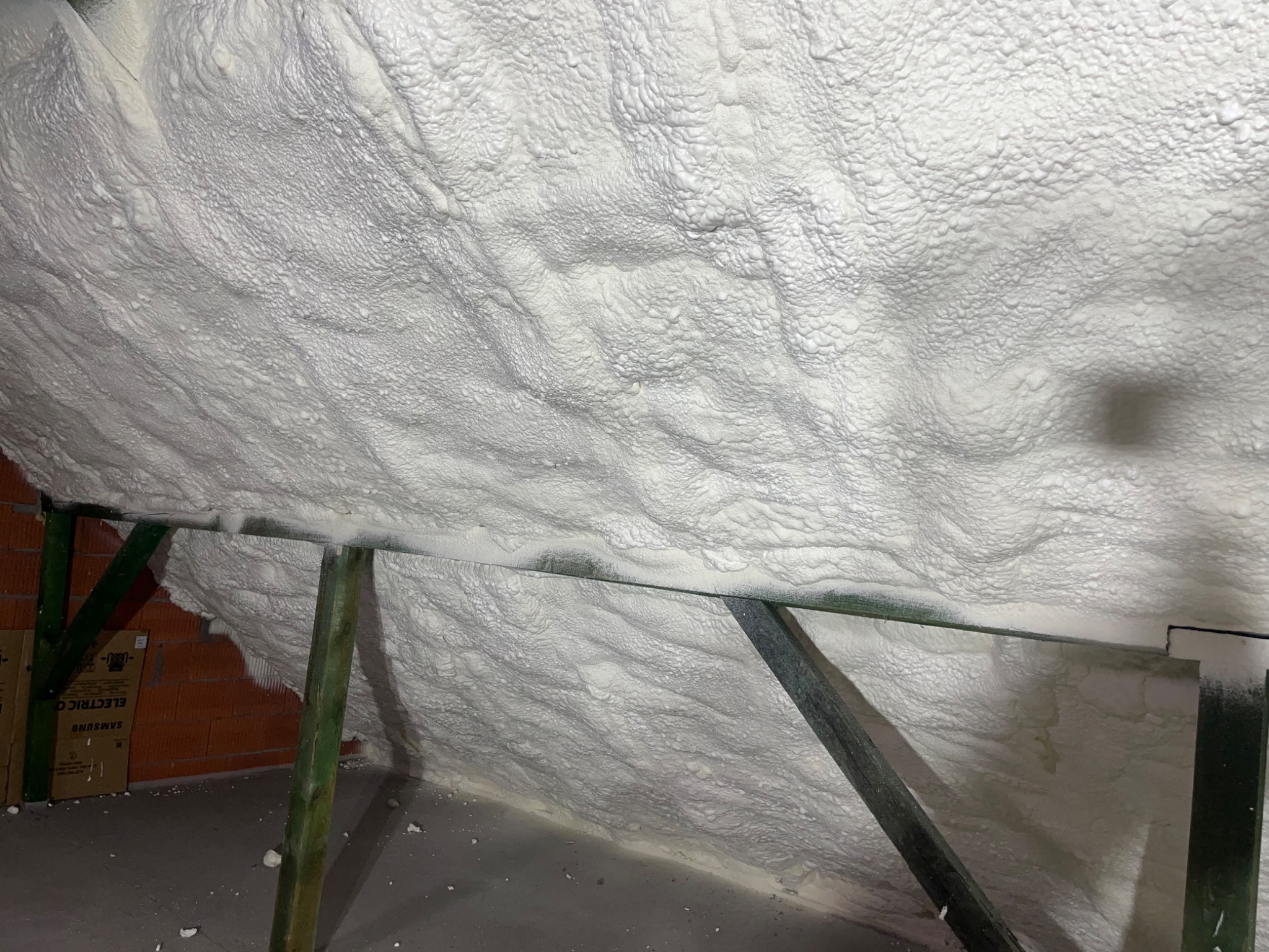 Poddasze po ociepleniu pianką PUR, widoczne drewniane elementy konstrukcyjne i faktura pianki. Biała, gęsta izolacja pokrywa skośne powierzchnie.