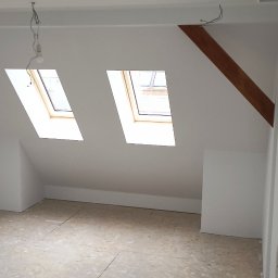 Djl.Gk.Pro Daniel Larek - Poddasze po remoncie z dwoma oknami dachowymi i surową podłogą z płyt OSB. Widoczne kable wystające z sufitu i fragment drewnianej belki.