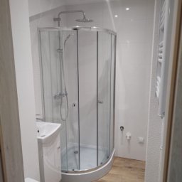 Djl.Gk.Pro Daniel Larek - Jasna łazienka po remoncie: kabina prysznicowa z hydromasażem, umywalka z szafką i toaleta. Drewnopodobna podłoga, białe płytki na ścianach. Nowoczesny design.