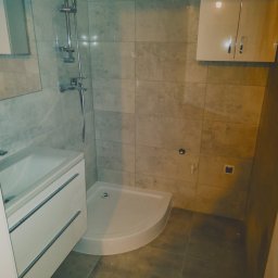 Djl.Gk.Pro Daniel Larek - Nowoczesna łazienka z kabiną prysznicową, umywalką z szafką i wiszącą szafką. Jasne płytki na ścianach i ciemniejsze na podłodze. Minimalistyczny design.