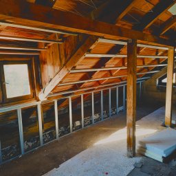 Djl.Gk.Pro Daniel Larek - Adaptacja poddasza: drewniana konstrukcja dachu z oknem, metalowe profile ścianek działowych, surowy beton i izolacja. Widok na wnętrze w trakcie prac.