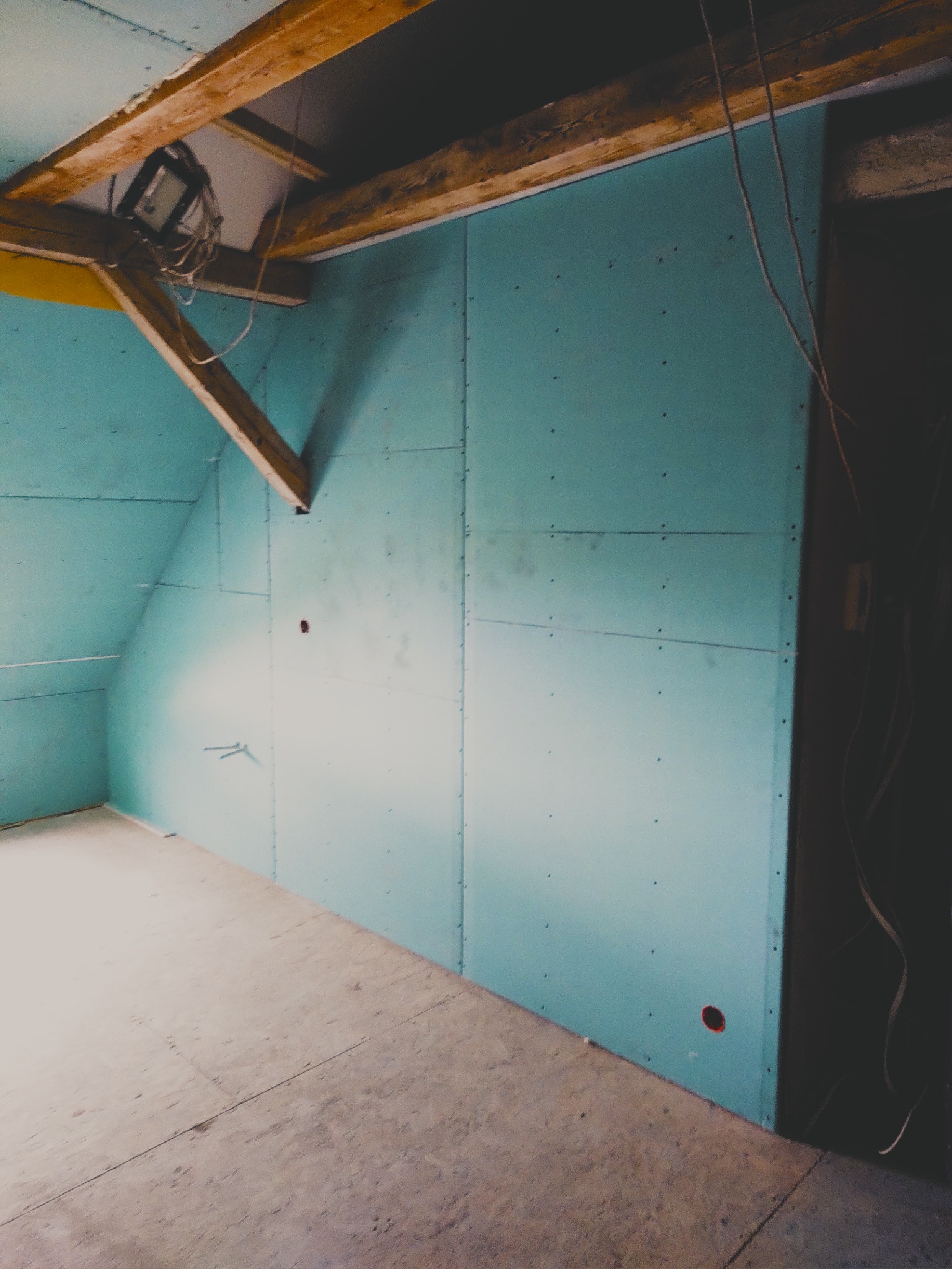 Poddasze z zamontowanymi płytami kartonowo-gipsowymi w kolorze turkusowym, widoczne drewniane belki stropowe i instalacja elektryczna.