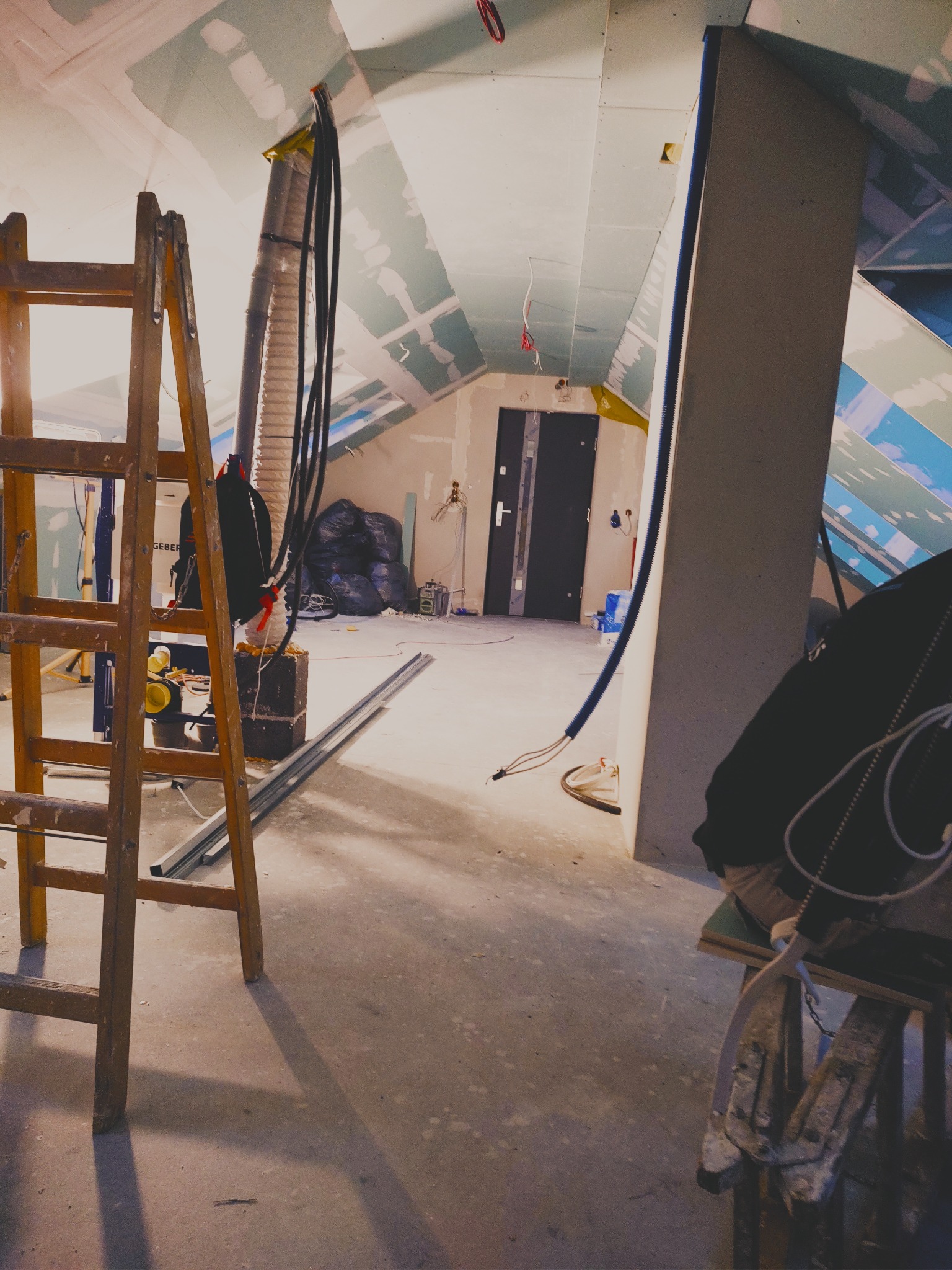 Montaż płyt karton gips w Miliczu. Widoczny stelaż, drabina i narzędzia. Sufit pod skosem z widocznymi łączeniami płyt. Prace wykończeniowe w trakcie realizacji.