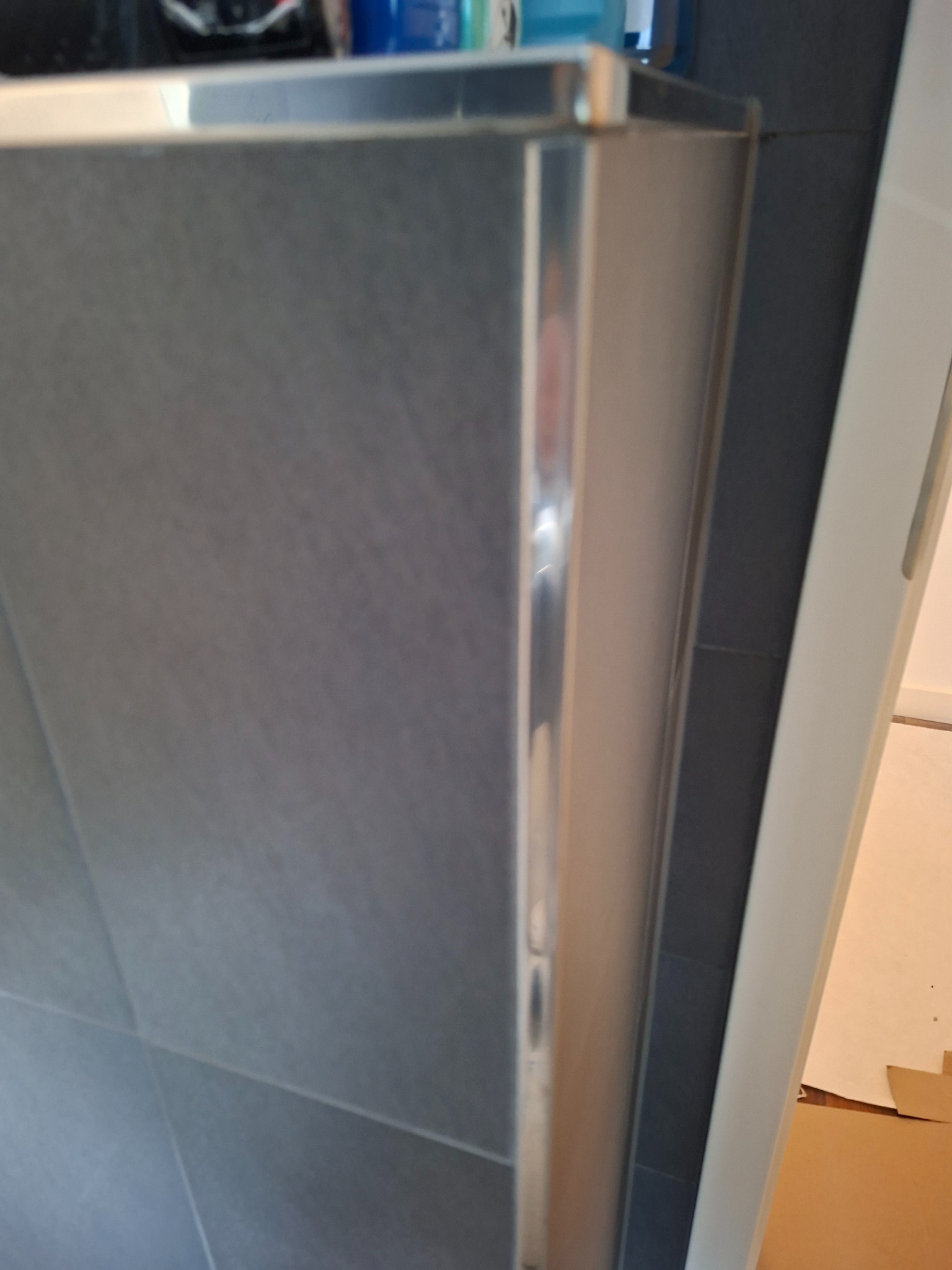 Szare płytki ceramiczne z metalową listwą wykończeniową, ułożone w łazience w Witnicy. Widoczny fragment futryny drzwi.