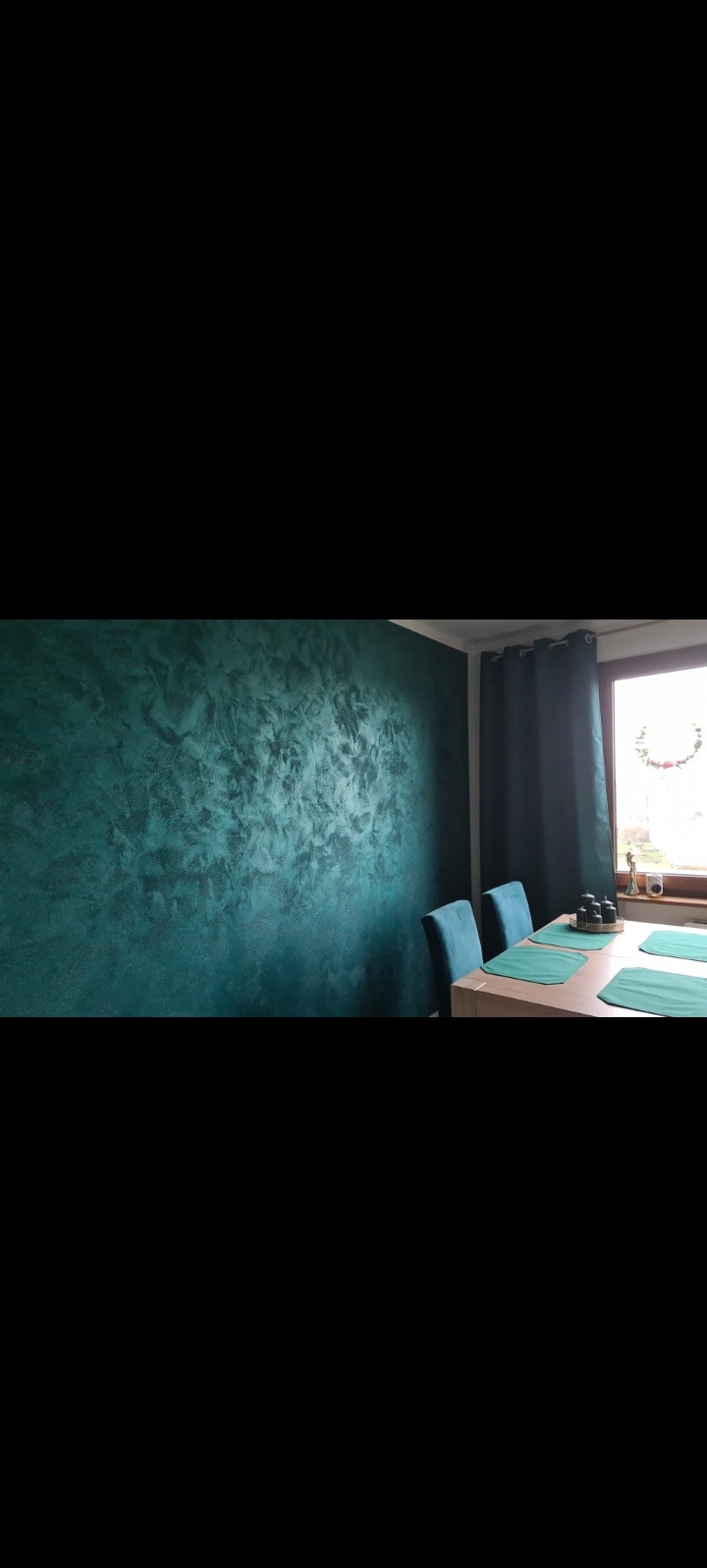 Dekoracyjna ściana w odcieniach zieleni z efektem aksamitu, widoczna z perspektywy jadalni z krzesłami i oknem w tle. Unikalna faktura i głębia koloru.