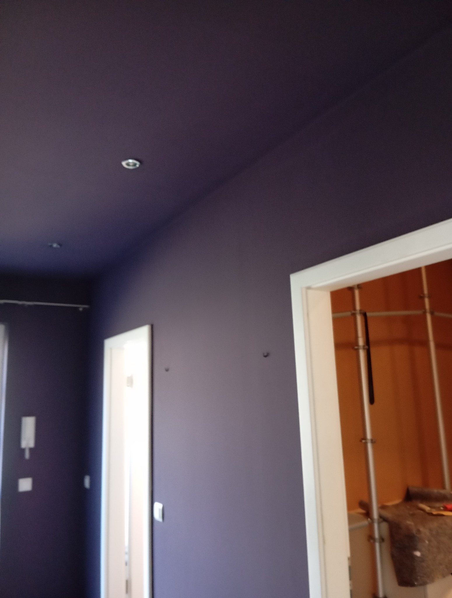 Fioletowe ściany i sufit z oświetleniem punktowym po malowaniu. Widoczne białe futryny drzwi i fragment wnętrza szafy.